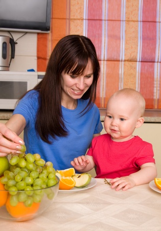 Beautiful happy mum with little son eat fruitの写真素材