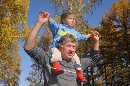Granddaughter on shoulders at the grandfather in autumn parkの写真素材