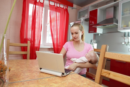 Woman with the laptop and the newborn on kitchenの写真素材