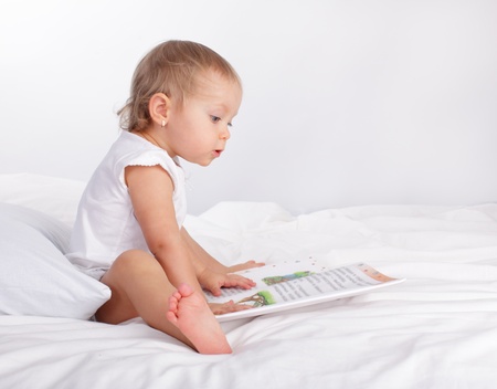 Baby reading book on the bedの写真素材