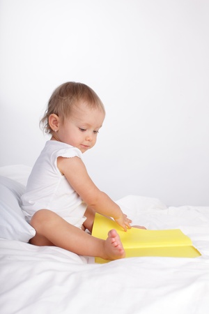Baby reading book on the bedの写真素材