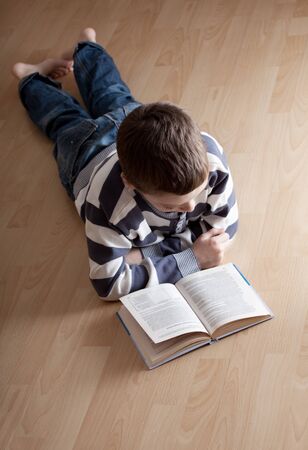 Child reading a book lying on the floorの写真素材