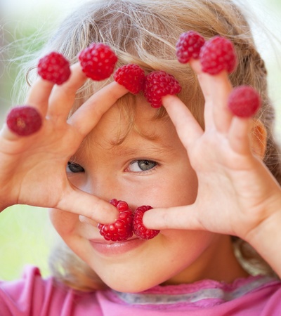 Happy little child with raspberry outdoors
