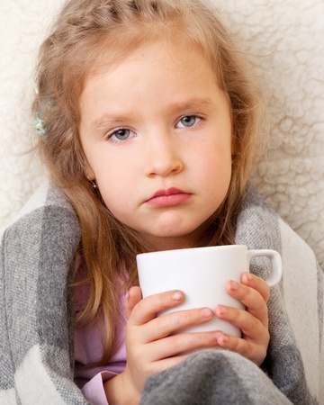 Illness child. Little girl wrapped in a blanket with mugの写真素材