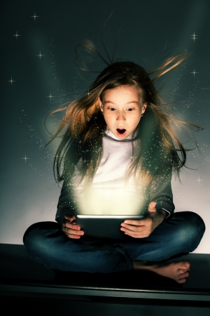 Surprised girl looking at a magic tablet. Child with tablet computerの写真素材