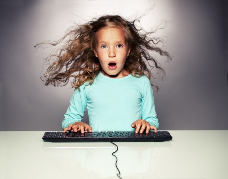 Surprised little girl with computer keyboard. Child looking at computer