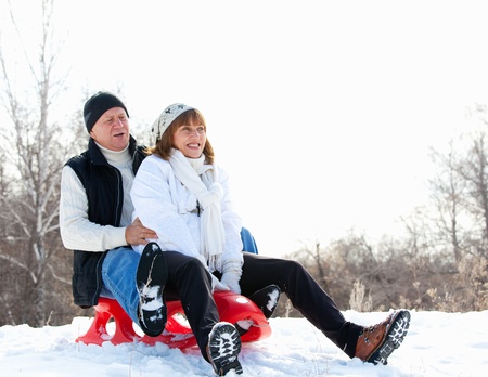 Mature couple sledding. Seniors couple on sled in winter parkの写真素材