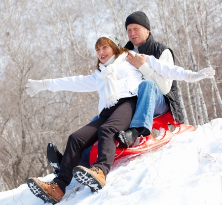 Mature couple sledding. Seniors couple on sled in winter parkの写真素材