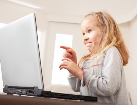 Surprised child with laptop indoors. Happy little girl playing computer at home.の写真素材