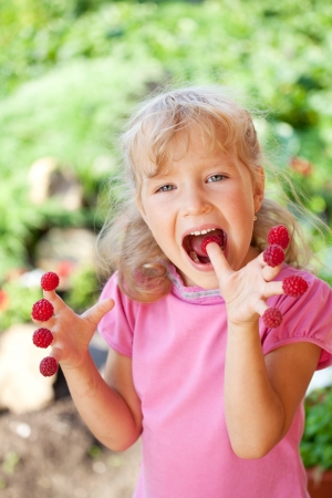 Happy little child with raspberry outdoorsの写真素材