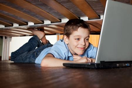 Child playing laptop under the bed. Computer Addictionの写真素材