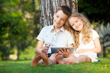 Children with tablet computer outdoors. Girl and boy playing at pc の写真素材