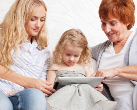 Family wiht tablet computer at sofa. Mother, grandmother and little girl at home on sofa. Generation