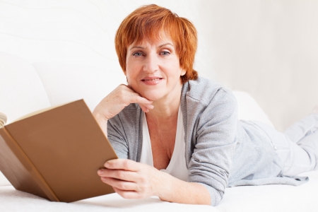 Adult woman reading book at sofa. Mature female at homeの写真素材
