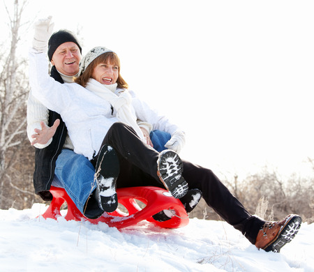 Mature couple sledding. Seniors couple on sled in winter parkの写真素材