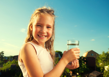 Girl holding glass with water. Happy child at summerの写真素材