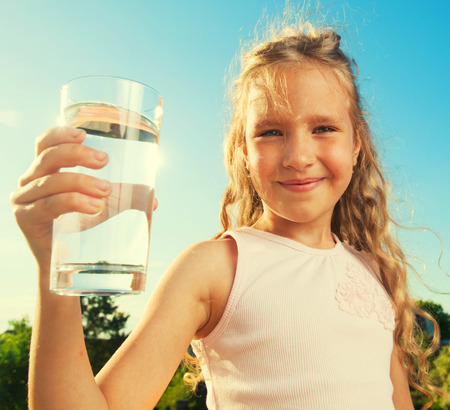 Girl holding glass with water. Happy child at summerの写真素材