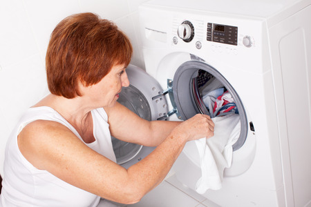 Woman puts clothes in the washing machine at homeの写真素材