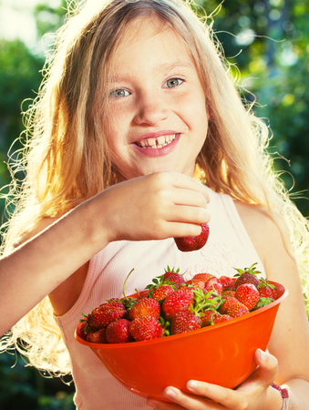 Child with strawberry. Girl with fruit, berry at gardenの写真素材