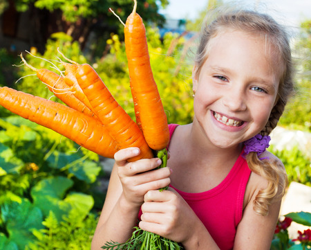 Child with carrot. Girl with vegetables in gardenの写真素材