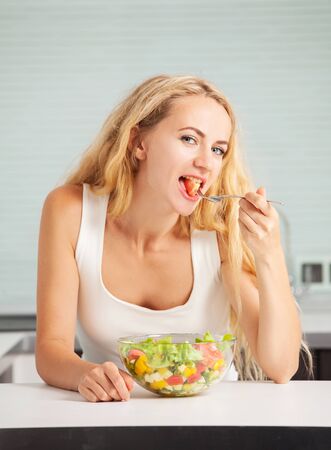 Young woman preparing vegetable salad in the kitchenの写真素材