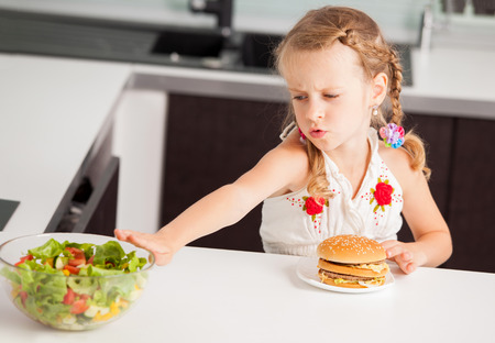 Child chooses between a healthy and unhealthy food. Girl with a hamburger and saladの写真素材