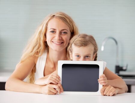 Female and child with a tablet. Family showing screen. Happy mother with girl at home
