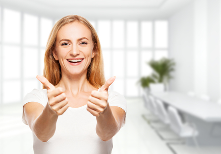 Happy businesswoman in the office. Young smiling female inside showing okの写真素材
