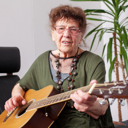 90 year old grandmother to play the guitar. Elderly woman at home. Mature female hobbiesの写真素材