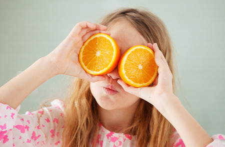 Cheerful girl with orange at home. Child with fruitの写真素材