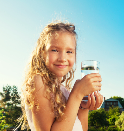Girl holding glass with water. Happy child at summerの写真素材