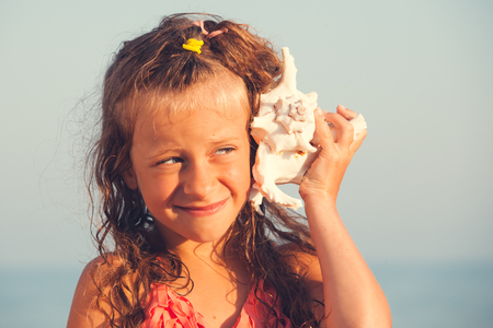 Child put the shell to her ear. Summer vacation. Girl on sea backgroundの写真素材