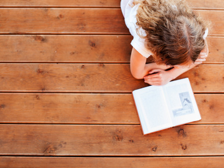 Child reading book at home. Girl lying and read indoors