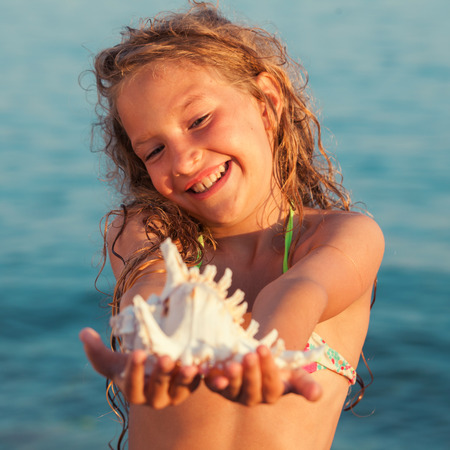Girl on sea background. Child put the shell to her ear. Summer vacation.の写真素材