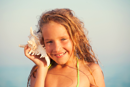 Girl on sea background. Child put the shell to her ear. Summer vacation.の写真素材