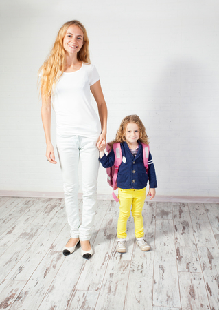 Mother helps her daughter get ready for school. Mom support child to wear a backpackの写真素材