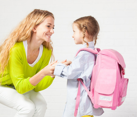 Mother helps her daughter get ready for school. Mom support child to wear a backpackの写真素材