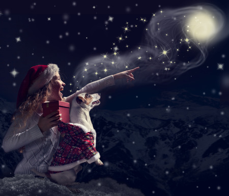 Happy child dog looks at the sky. Girl and pet in christmas hat with giftの写真素材