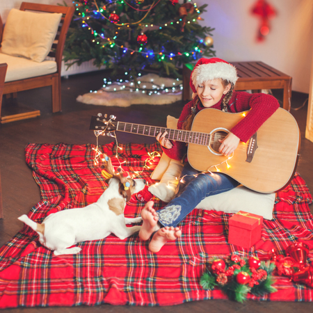 Girl with a dog playing the guitar and singing near christmas tree. Happy New Yearの写真素材
