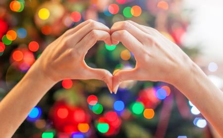 Heart from the hands in front of  christmas treeの写真素材