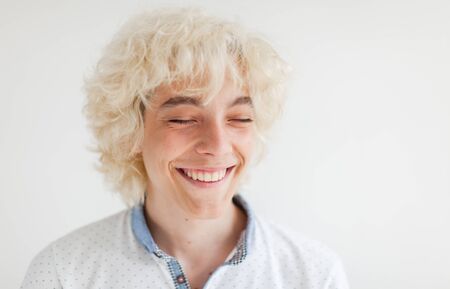 Portrait of cheerful young blond man smiling looking at camera. Happy teen at studioの写真素材