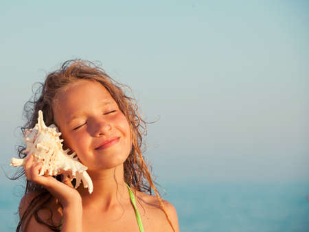 Girl on sea background. Child put the shell to her ear. Summer vacation.の写真素材