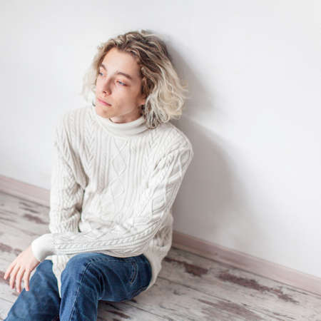 Sad young man sitting near the wall. Unhappy teen at home Stressの写真素材