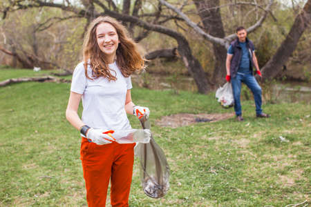 People collect garbage and plastic bottles in the forest. Man and girl clean park of garbage Global...