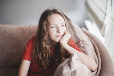 Expression of lonely female teenager at home. Portrait of a sad teenage girl looking thoughtful about troubles. Pensive teen. Depression, teen depression, pain, suffering, stressの写真素材