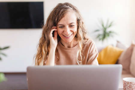 Laughing happy casual beautiful woman working on a laptop at home Smiling freelancer female looking...