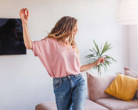 Caucasian young happy joyful woman dancing in modern living room in house alone listening to music making moves and having fun. Rhythm concept, home dancerの写真素材