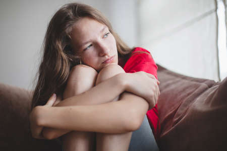 Sad thoughtful teen girl sits on couch feels depressed, offended or lonely, upset young woman...