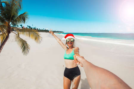 Girl on the beach in a New Year's hat holds a glass of champagne in her hand. Happy woman celebrates Christmas on the ocean coastの写真素材