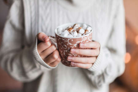 Warming cup of coffee in the hands of women. Girl warms up in cold winter weather with hot chocolate or cocoa with marshmallowsの写真素材